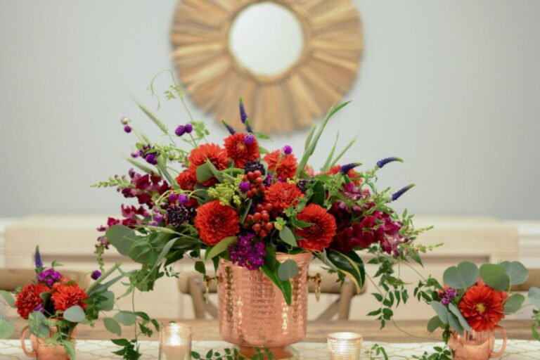 Mesa decora com arranjos de flores vermelhas em vasos dourados.